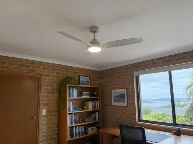 White ceiling fan on a plaster ceiling in a brick-walled room with window and desk in Avoca Beach