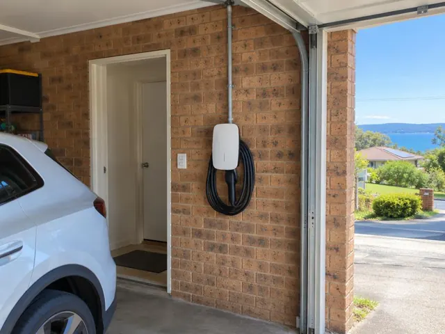 Wall-mounted EV charger on a brick garage wall beside a driveway and doorway in Copacabana